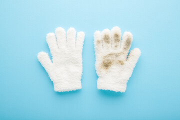 Clean and dirty child white warm gloves on light blue table background. Pastel color. Compare two objects. Closeup. Top down view.