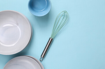 Plates, bowl and whisk on a blue background. Set of dishes. Top view, copy space