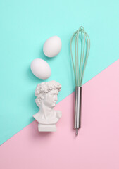 Culinary minimal flat lay still life. Bust of David, eggs and whisk on a blue-pink pastel background. Top view