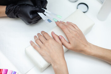 Obraz na płótnie Canvas Manicurist selects the color of manicure for the nails of a female client in a nail salon