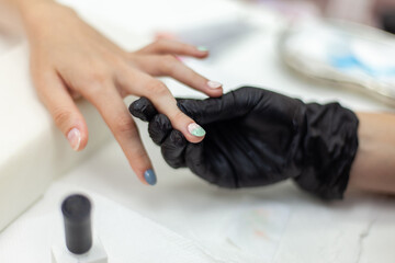 Manicurist paints with nail polish the nails of a woman's clint in nail salon. The working process