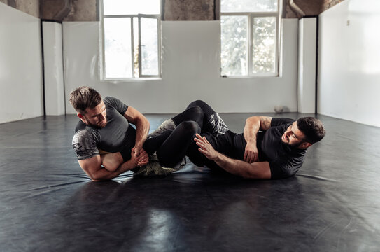 Two athletic male fighters are training, practicing a painful hold in a sports hall.
