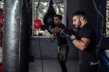 Athletic boxers practice punching in gloves with a punching bag in a sports hall