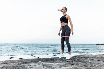 Young beautiful fit woman in sportwear training with a fitness elastic band (expander) on a urban...