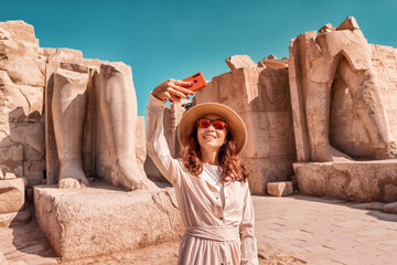 A blogger girl takes a selfie against the ruins of the grandiose Karnak temple in the ancient city...