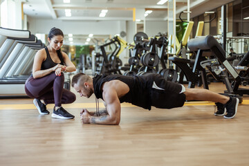 Fototapeta na wymiar Athletic man doing plank exercise and beautiful girl timed in the gym