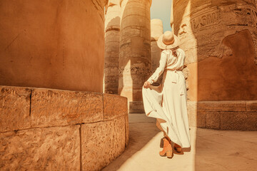 Woman traveler explores the ruins of the ancient Karnak temple in the city of Luxor in Egypt. Great row of columns with carved hieroglyph - obrazy, fototapety, plakaty
