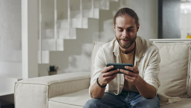 Positive guy relaxing on couch with smartphone in hands