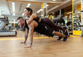 Strong man doing push-ups with a woman on his back in the gym