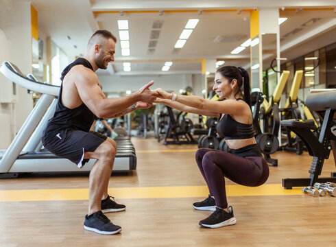 Athletic man with woman squats holding hands in the gym. Workout together .