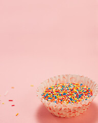 Cupcake liners with colored sugar inside and near it. Confectionery cooking concept with copy space on pink bright paper background. National cooking day.