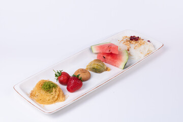 View of Güllaç dessert, watermelon slices, pistachio baklava, Şekerpare dessert, strawberries and kadayif dessert, shot from the opposite angle, on white background in an isolated setting.