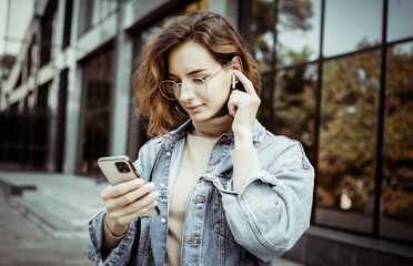 Modern woman in stylish clothes using smartphone outdoors in the city