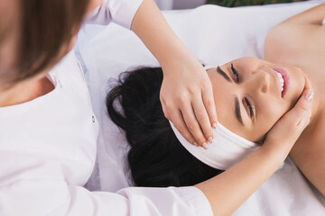 Fototapeta na wymiar Above photo of cosmetologist making facial beauty massage treatment for relaxed young woman face with fingers movements in beauty spa salon.