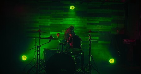 Fototapeta na wymiar Professional drummer playing on stage during rock show in green spot lights