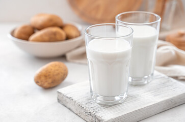 Vegetable potato milk on a white background with raw potatoes. An alternative to cow's milk. Side view, copy space.