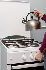 female hand puts a metal kettle on a gas burner