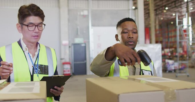 Diverse male workers wearing safety suits and scanning boxes in warehouse