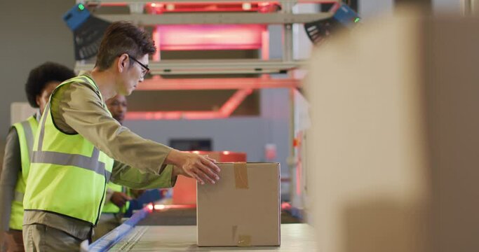 Diverse male and female workers wearing safety suits with boxes on conveyor belt in warehouse