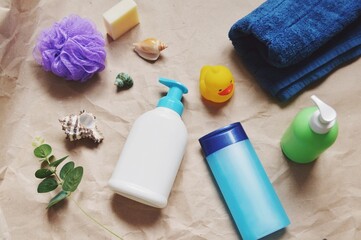 Purple sponge, shampoo bottle, shower gel, liquid soap, green eucalyptus branch, rubber duck and fluffy towel. Natural spa cosmetics for hair and skin care flat lay photography 