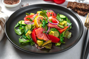 Salad with salmon, fresh vegetables and herbs close-up on a gray background. Side view. Healthy, dietary food.