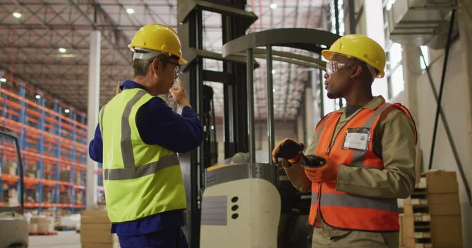 Diverse male workers wearing safety suits and talking in warehouse