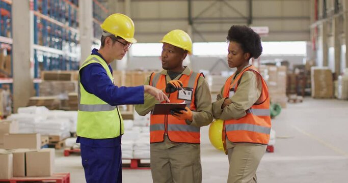 Diverse male and female workers wearing safety suits and talking in warehouse