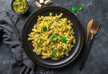 Fusili pasta with pesto sauce, sesame seeds and fresh basil on a dark background. Top view.