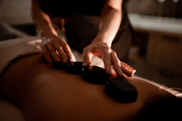 The masseuse massages the girl's back with hot stones. Hot stone massage in the spa.