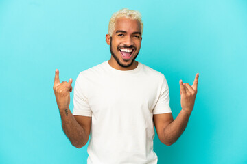 Fototapeta premium Young Colombian handsome man isolated on blue background making horn gesture