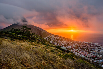 A dramatic sunset over Cape Town with the Lion's Head summit in clouds. - obrazy, fototapety, plakaty