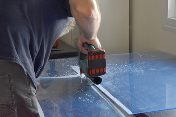 Man using a cordless jigsaw tool to cut acrylic sheet. Work from home concept.  - obrazy, fototapety, plakaty