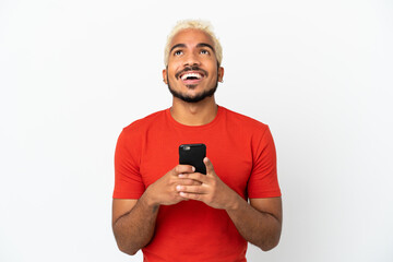 Young Colombian handsome man isolated on white background using mobile phone and looking up