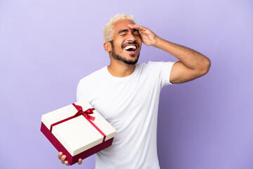 Young Colombian man holding a gift isolated on purple background smiling a lot