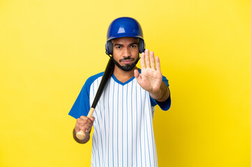 Young Colombian latin man playing baseball isolated on yellow background making stop gesture