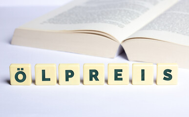 Das Wort Ölpreis in Buchstaben mit geöffnetem Buch im Hintergrund