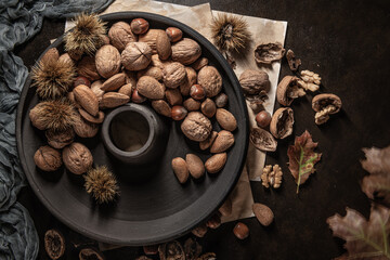Obraz na płótnie Canvas Modern design black ceramic bowl with walnuts, hazelnuts, almonds, chestnut hedgehogs on dark countertop and background. Autumn table