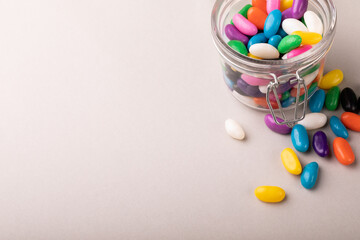 High angle view of copy space with colorful candies and open glass jar on white background
