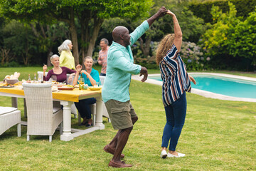 Multiracial senior couple dancing while friends at table in background during backyard party © wavebreak3
