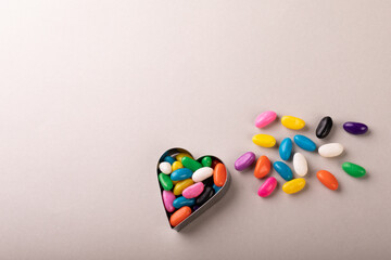 Overhead view of heart shape container with colorful candies by copy space on white background