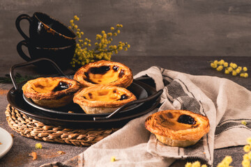 Traditional Portuguese pastry Pastel de Nata or Pastel de Belém served with cinnamon powder in a traditional tray on a rustic board. Egg tart