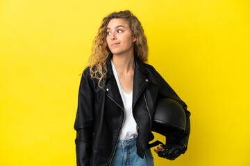 Young blonde woman with a motorcycle helmet isolated on yellow background looking to the side