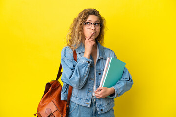 Young student caucasian woman isolated on yellow background having doubts while looking up