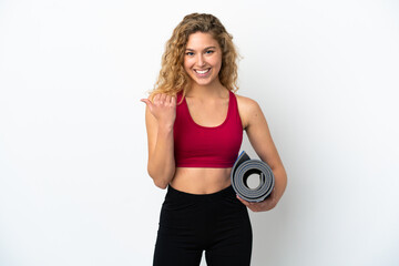 Fototapeta premium Young sport blonde woman going to yoga classes while holding a mat isolated on white background pointing to the side to present a product
