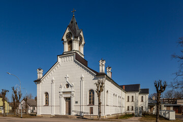 Naklejka premium Sloka Evangelical Lutheran church in Jurmala, Latvia during early spring day. White Lutheran church at bright sunny spring day. White stone chapel at blue sky background.