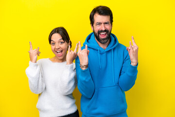 Young caucasian couple isolated on yellow background making rock gesture