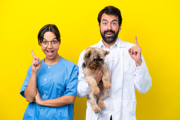 Young veterinarian couple with dog isolated on yellow background pointing up a great idea