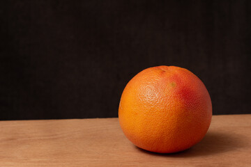 photo of a ripe juicy orange on a wooden cutting board on a dark background with empty space