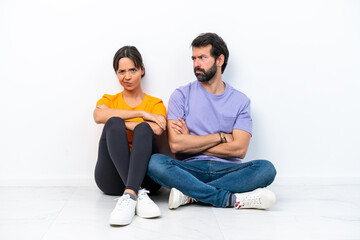 Fototapeta na wymiar Young caucasian couple sitting on the floor isolated on white background annoyed angry in furious gesture
