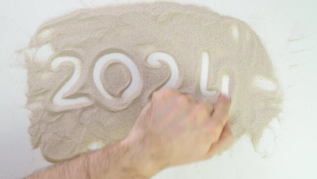 2024 text Top view draw on the sand. Caucasian hands write text in beige sand. Vacation and travel. Beach on vacation. Sand painting. Creativity from natural materials.